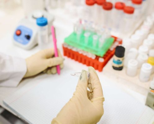 Lab technician handling a sample vial with test tubes and tools in the background